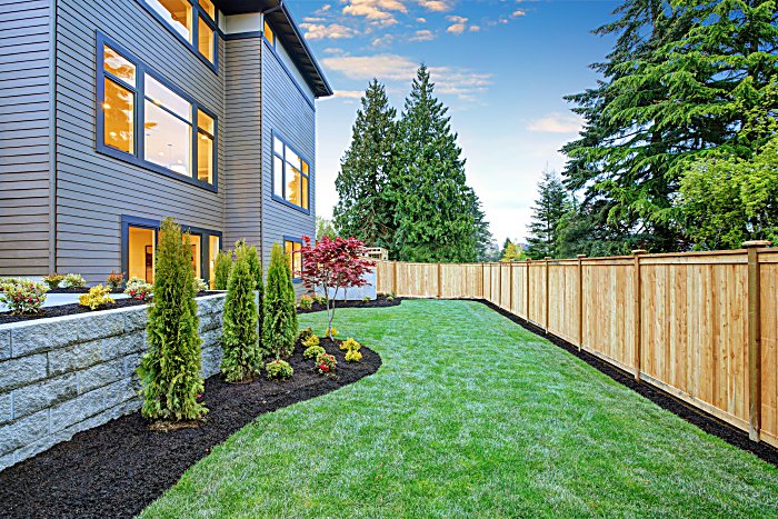 Luxurious contemporary three-story wood siding home exterior. Nice backyard landscape with well kept lawn, flower beds and wooden fence.