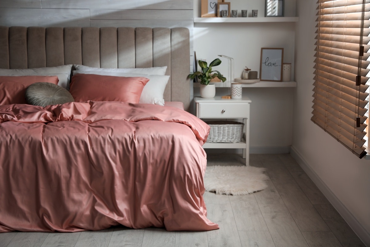 Bed with beautiful silky linens in stylish room interior