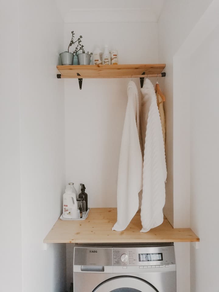 Freshly laundered towels hanging from wooden clothes rod above washing machine
