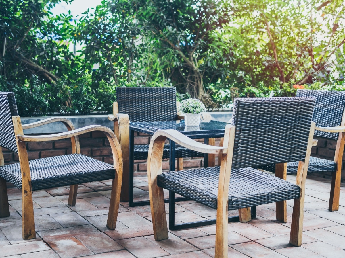Four outdoor woven armchairs and glass table on brick floor near the garden