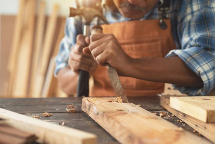 Asian senior carpenter using a chisel and hammer to carve wood in a workshop 