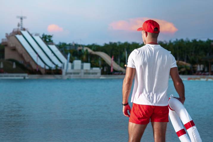 A male lifeguard on the beach holds a lifebuoy in his hands