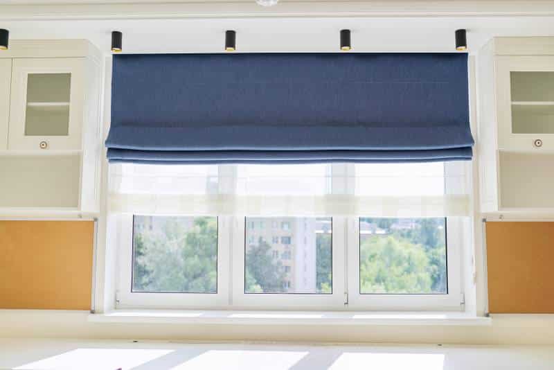 Roman blind in the interior, close-up. Curtain blue blackout fabric, sheer white linen, yellow wall