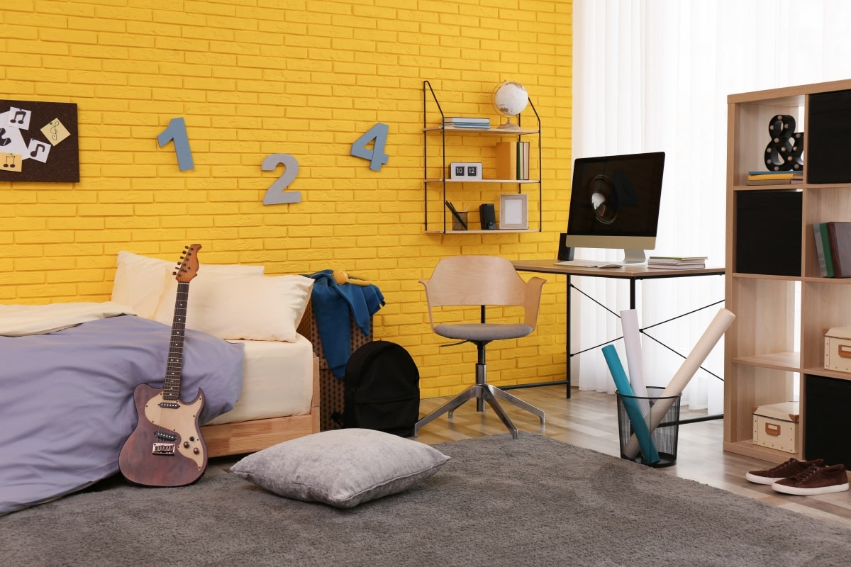 Teenager's room interior with computer, bed, and yellow walls