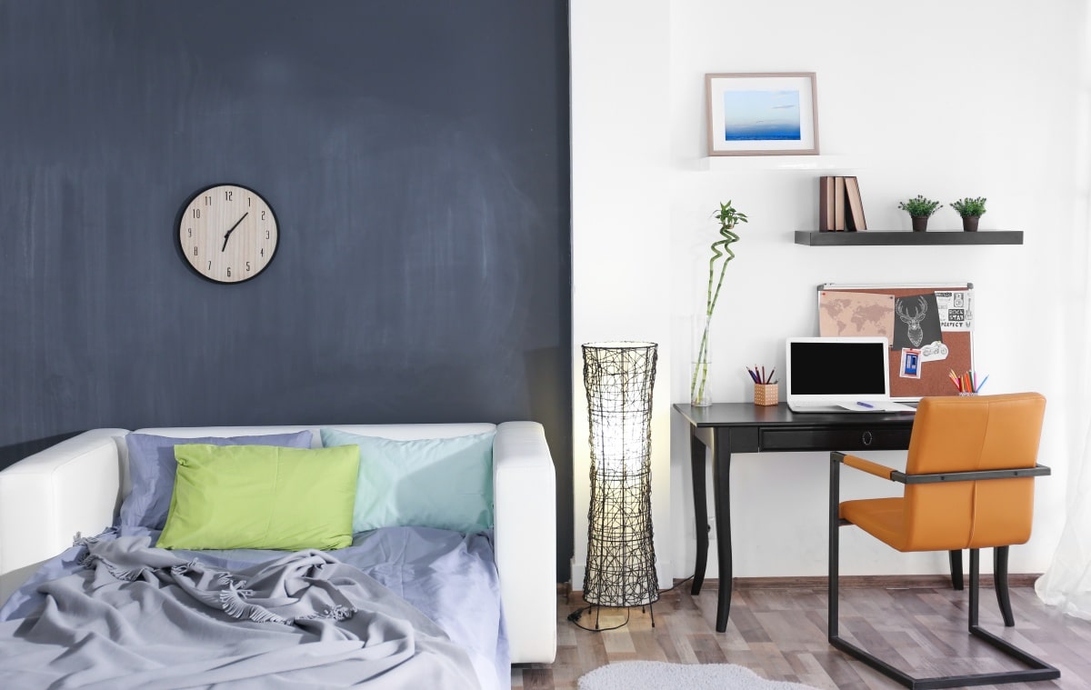 White bed and wooden desk in bedroom with wooden floor and two textured walls