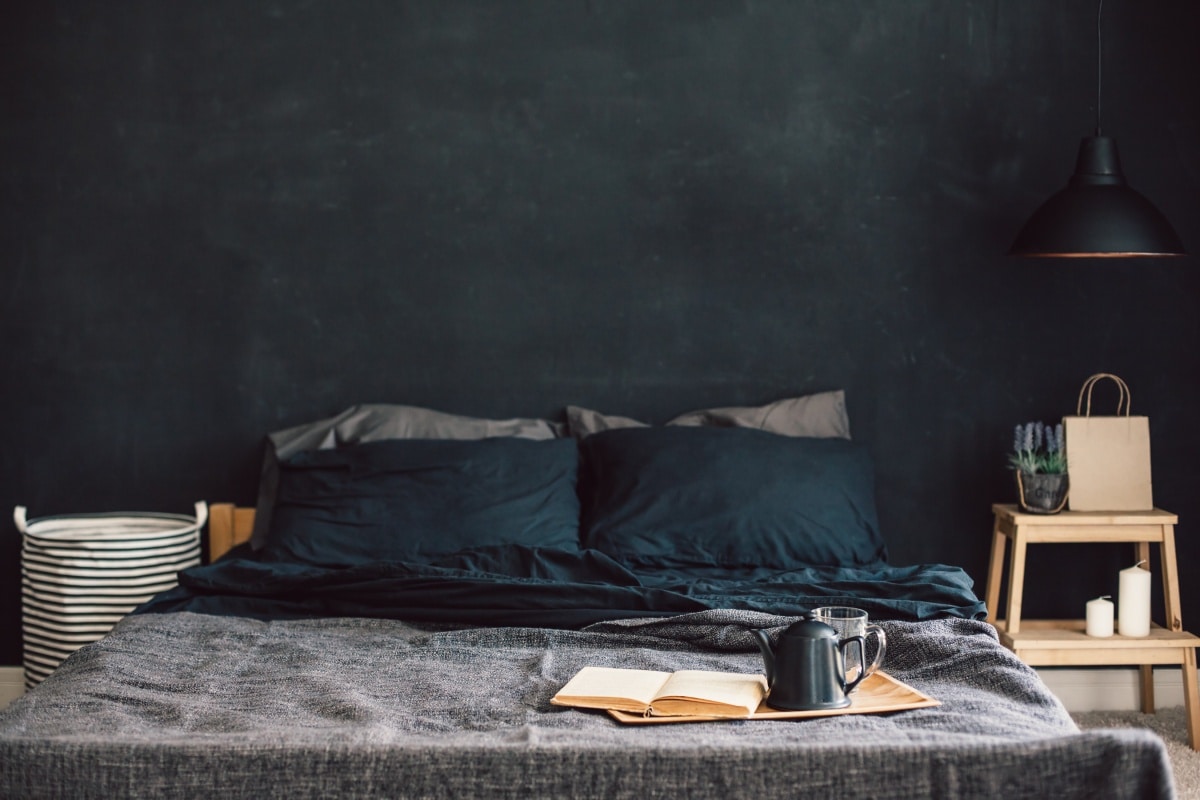 Unmade black bed with breakfast and book on tray