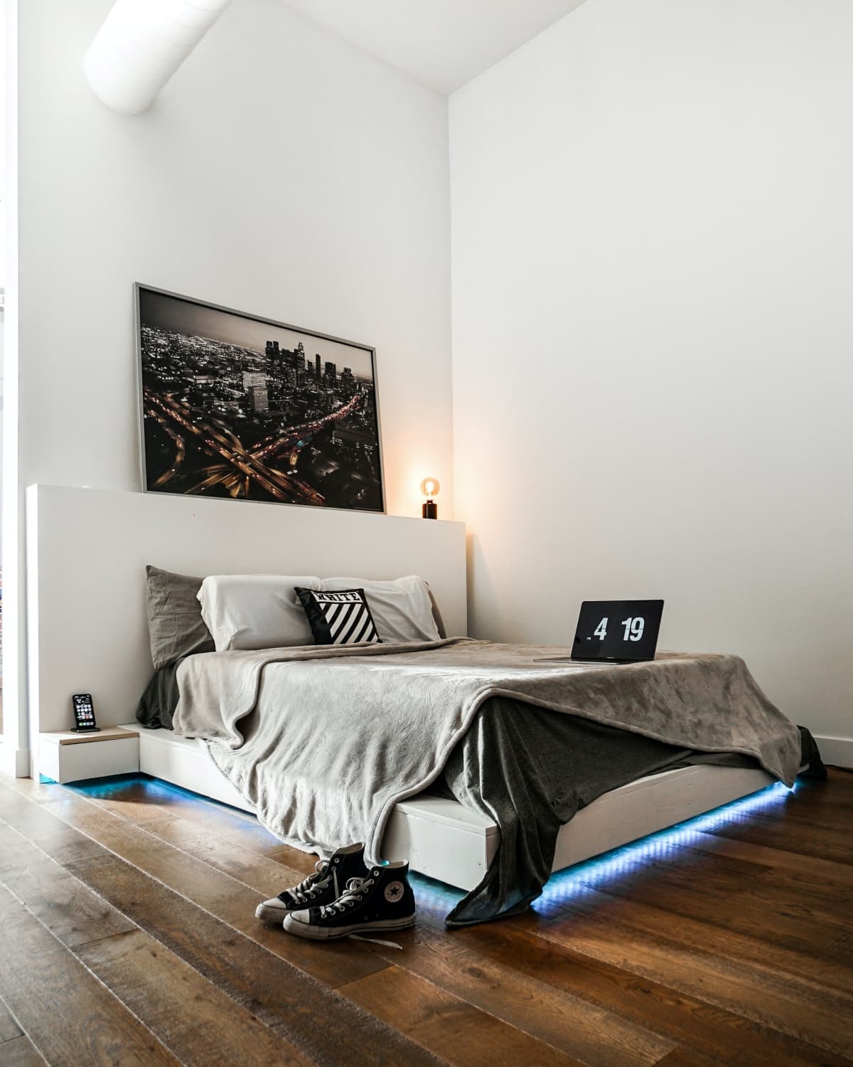 Blue neon lighting under a bed with a laptop and grey bedding