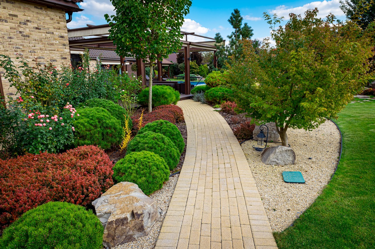 yard landscape design with multicolored shrubs intersecting with bright green lawns behind a house