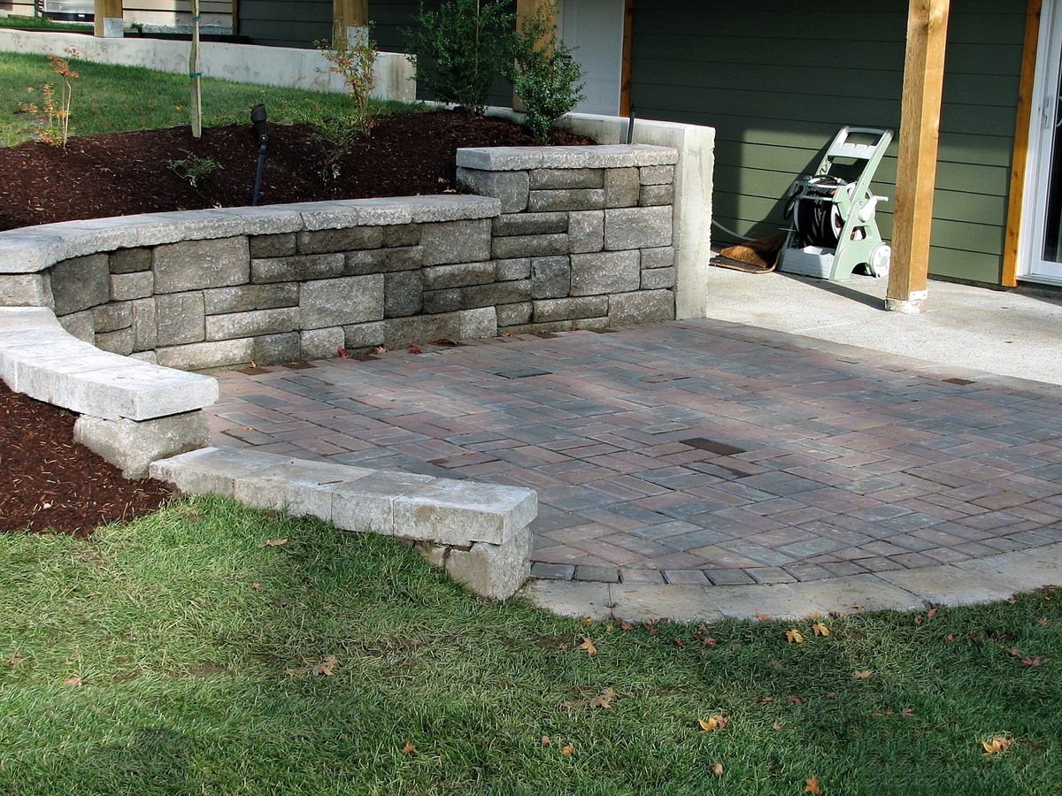 retaining wall staggered concrete blocks with patio pavers on patio deck surrounded by lawn grass and planted area in close-up view