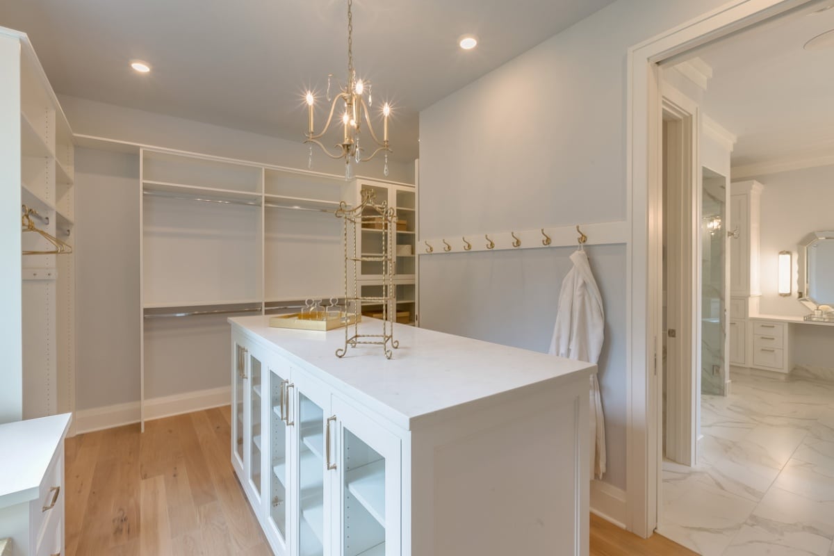 island dresser in an empty walk in clsoet with gold handles, racks, display stands, and chandelier