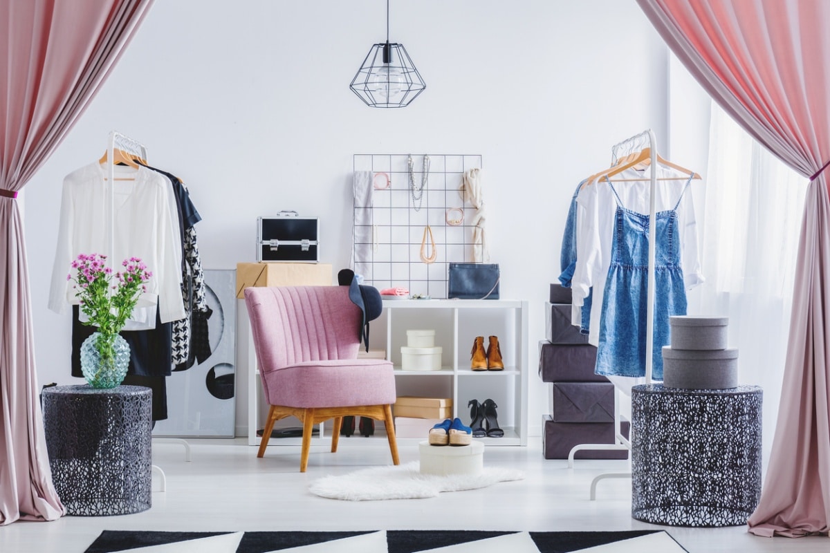 Pink chair in dressing room with flowers on designer table and clothes on hangers