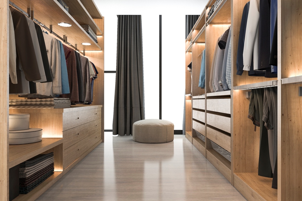 walk-through closet with light wood floors and cabinets and an ottoman near a window