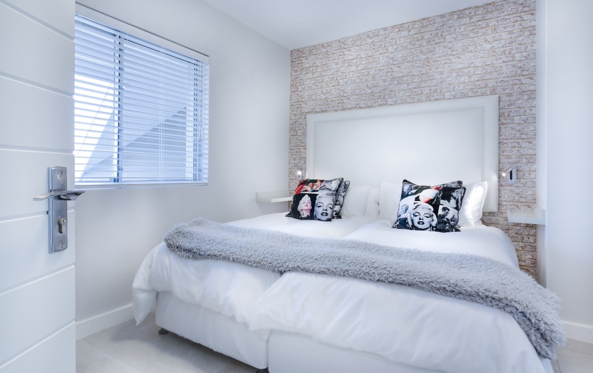 White and grey quilt and Manilyn Monroe printed pillows on a bed with a plain white headboard