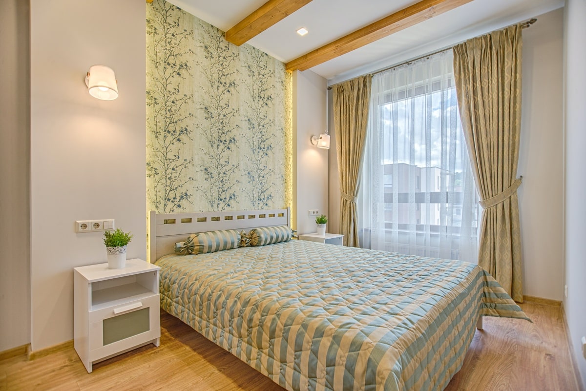 Bed with striped bedding with a leaf-patterned feature wall behind it