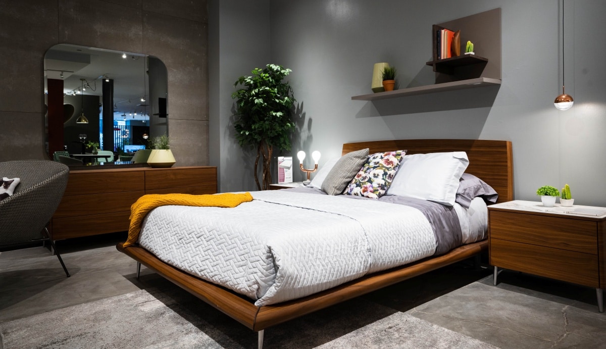 Bed with a dark wood bedframe and headboard in a dimly lit room with grey walls