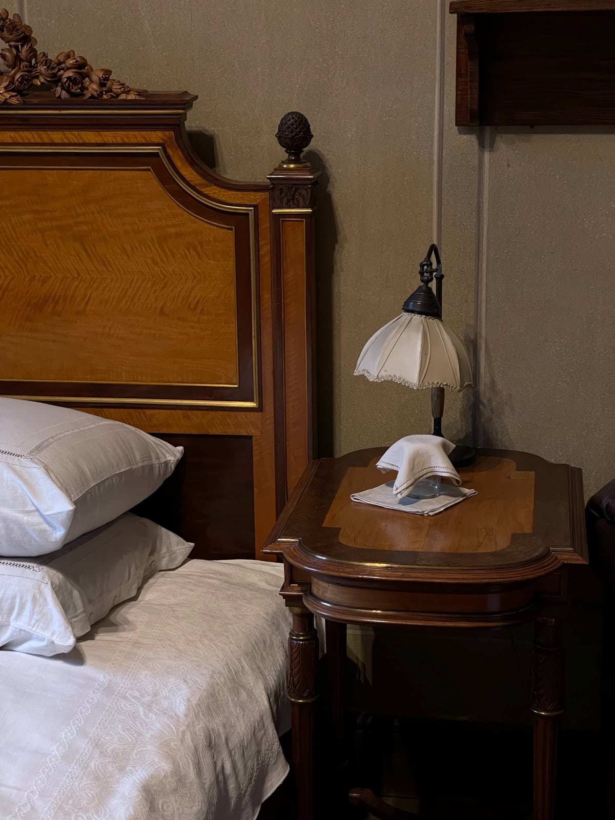 Vintage table and lamp near vintage wooden bedframe and bed with white pillows and sheets