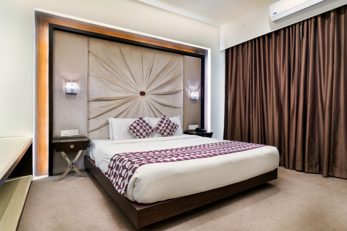 White and maroon bedroom with big cushioned statement headboard and long curtains