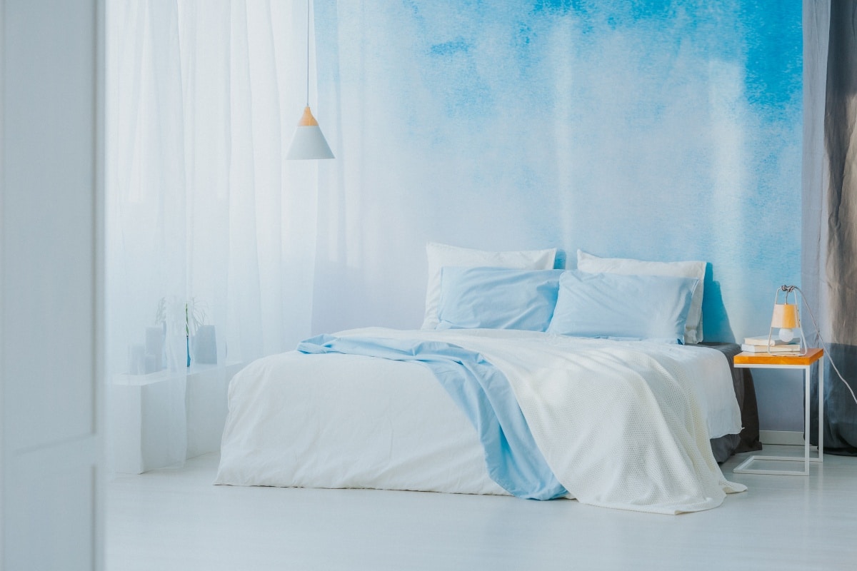 Side angle of king size bed next to a wooden side table and blue wallpaper