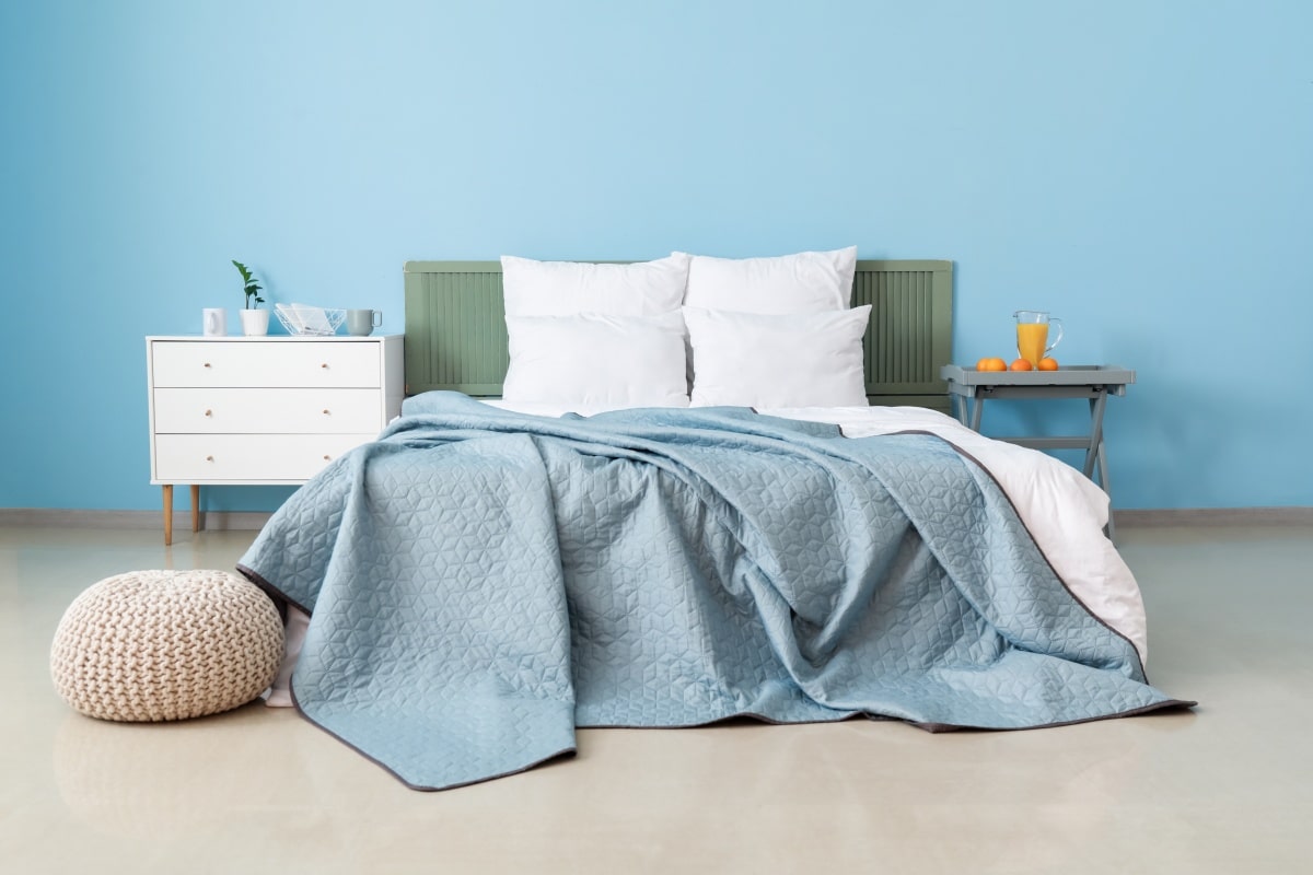 Double bed near color wall in interior of stylish baby blue coloured bedroom
