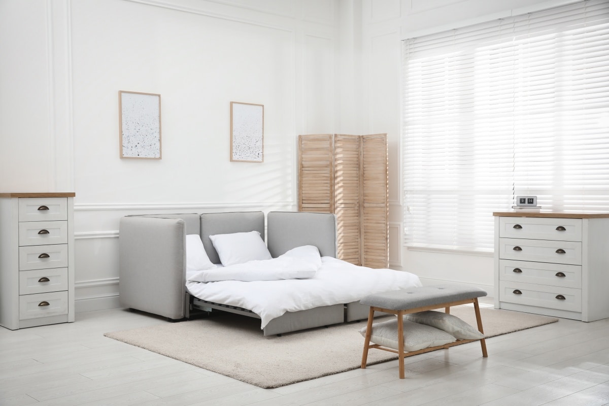 Stylish room interior with sleeper sofa near white wall