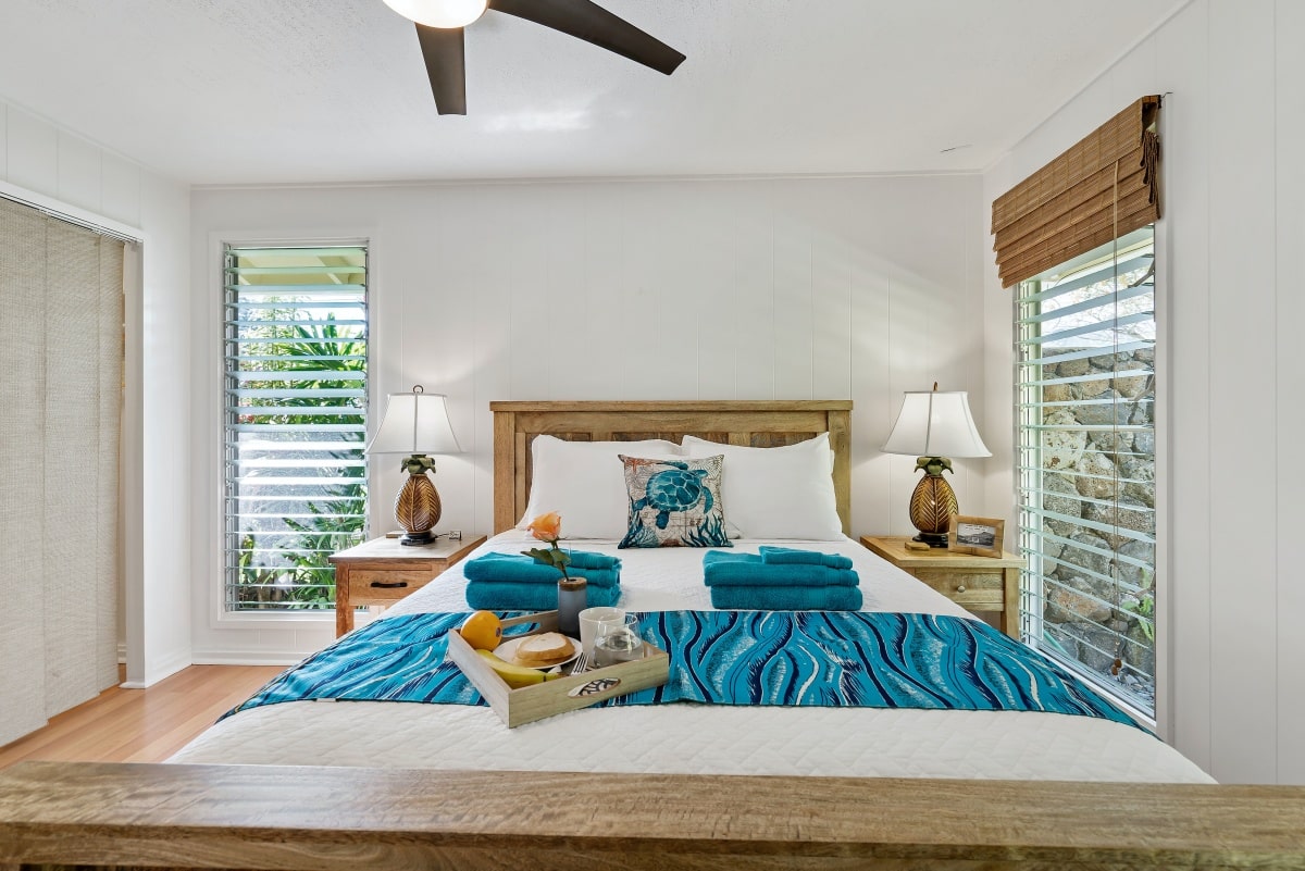 bedroom with louvred windows, tray of food on a bed with blue sheets, and ceiling fan