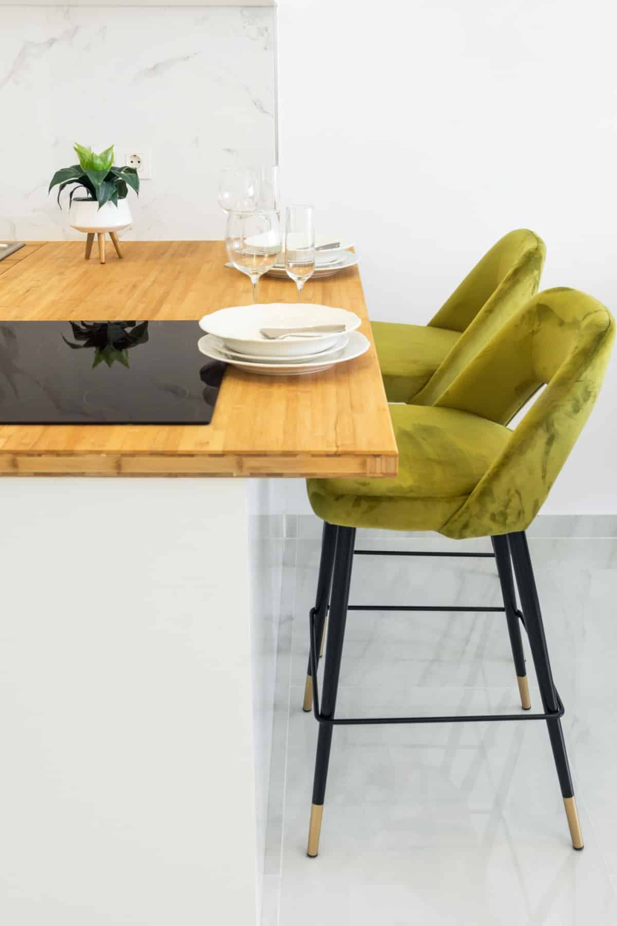 Modern minimalist open kitchen interior with wooden countertop vitroceramic cooking surface table setting with plates glasses high stools on white wall background