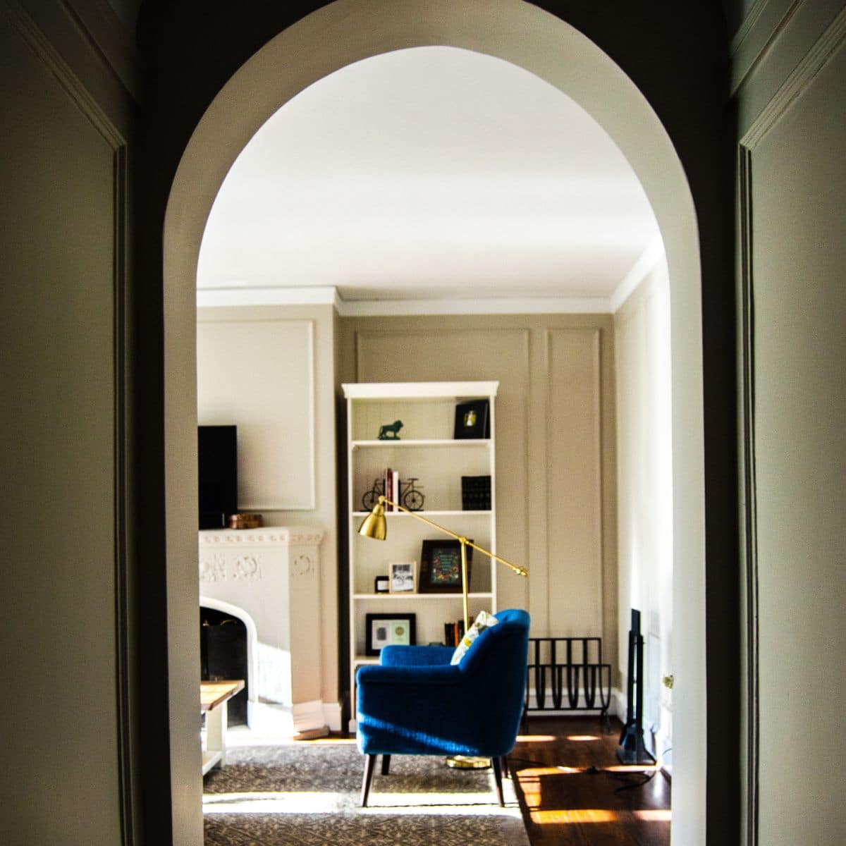 A hallway with a bookshelf, a blue chair, and a gold lamp