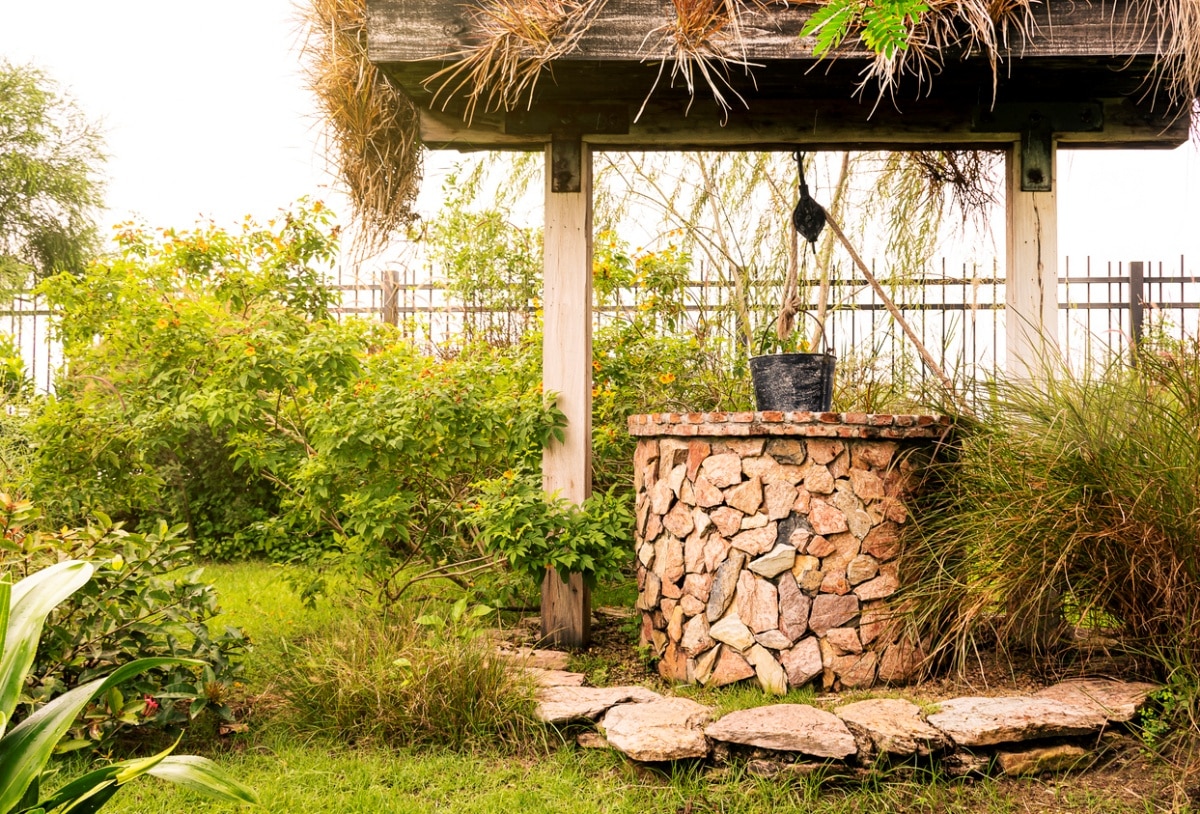 Vintage stone brick well with black steel bucket in garden