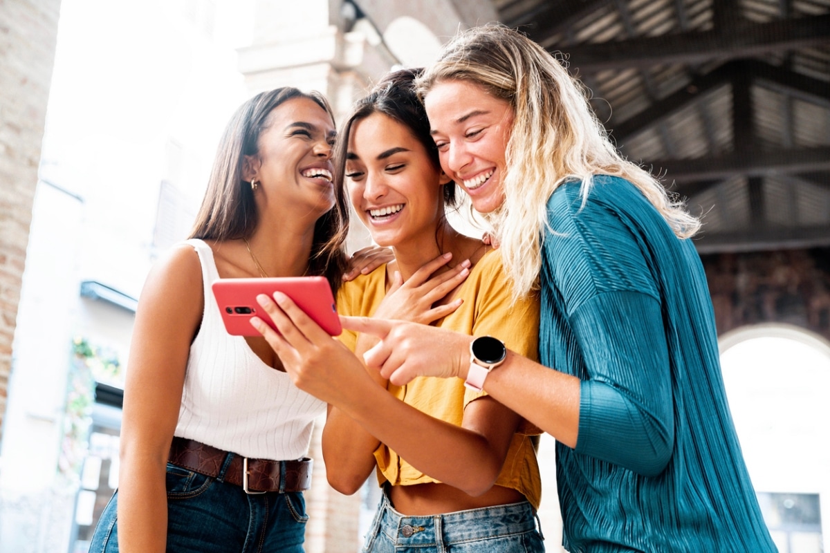 Three happy friends watching a viral video trend on a smartphone