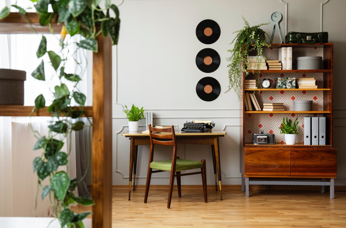 Black retro typewriter on a unique wooden desk, a mid-century modern chair and a renovated bookcase in a hipster home office interior.