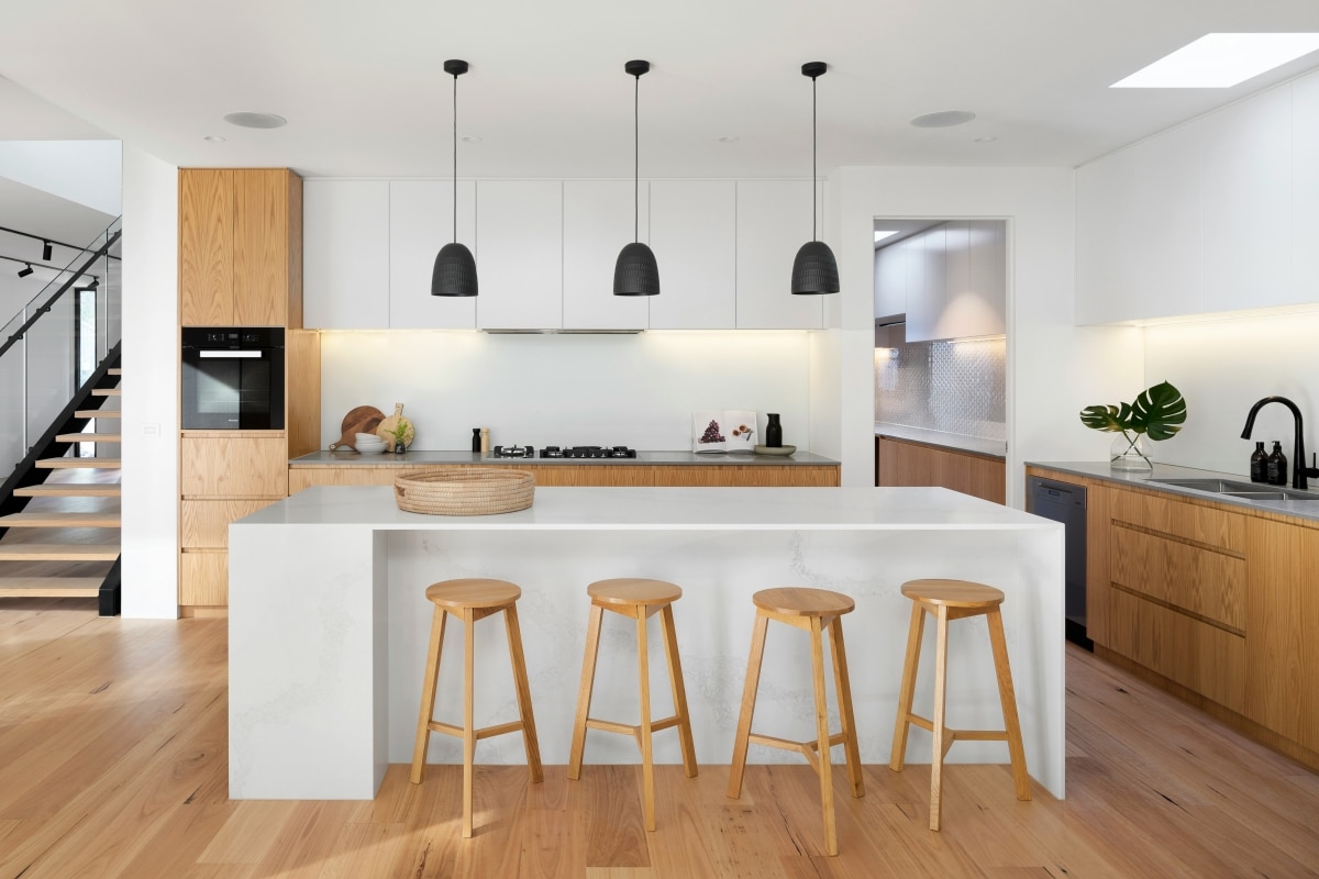 Modern kitchen showcasing a minimalist hidden kitchen design with a sleek island, natural wood cabinets, black pendant lighting, and an open layout.