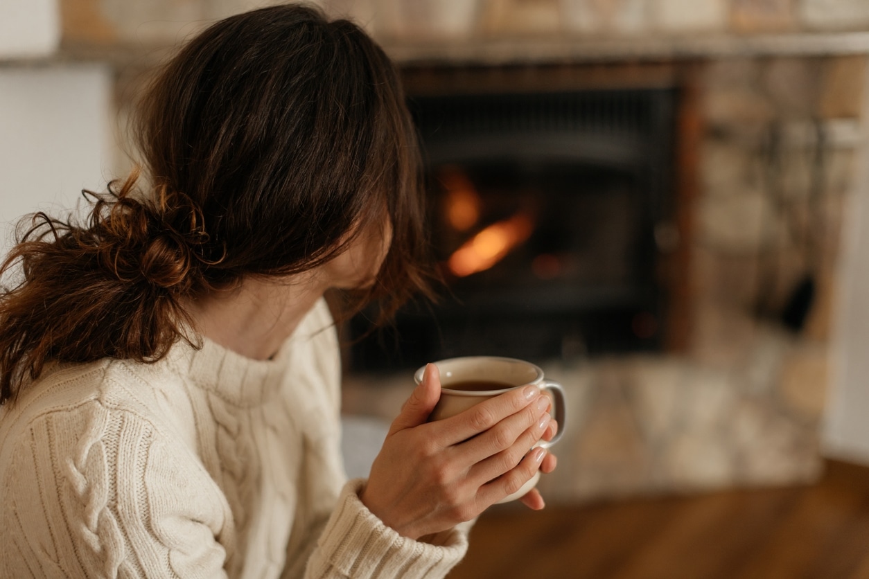A woman sitting by the fireplace, drinking her cup of tea.